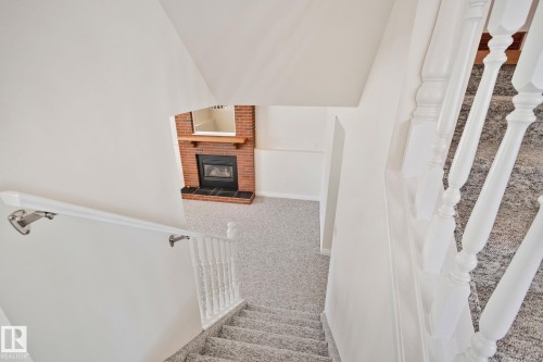 Carpeted staircase with white balusters leading to a room featuring a brick fireplace with a wood mantle and black hearth - 18903 70 Avenue, Edmonton, AB - Indoor