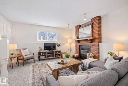 Spacious living area featuring a prominent brick fireplace with a wood mantel, a built-in firebox, and a hearth - 18903 70 Avenue, Edmonton, AB - Indoor Photo Showing Living Room With Fireplace