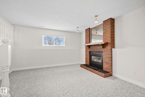 Brick fireplace with a black insert and hearth, featuring a wood mantel - 18903 70 Avenue, Edmonton, AB - Indoor Photo Showing Other Room With Fireplace
