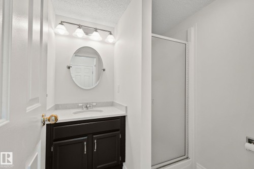 Bathroom featuring a dark wood vanity with a white countertop and an oval mirror, illuminated by a four-bulb vanity light fixture - 18903 70 Avenue, Edmonton, AB - Indoor Photo Showing Bathroom