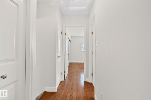 Hallway featuring wood-finish flooring, white paneled doors, white walls, and a recessed ceiling detail - 18903 70 Avenue, Edmonton, AB - Indoor Photo Showing Other Room