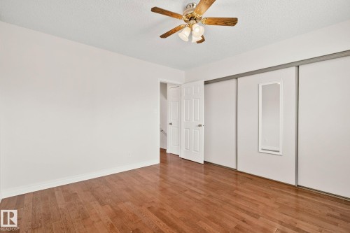 Bedroom featuring wood-finish flooring, a ceiling fan with integrated lighting, and white sliding closet doors - 18903 70 Avenue, Edmonton, AB - Indoor Photo Showing Other Room