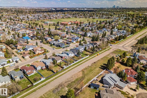 Aerial perspective showcasing a residential neighborhood with diverse housing styles, mature trees, and a distant city skyline - 18903 70 Avenue, Edmonton, AB - Outdoor With View