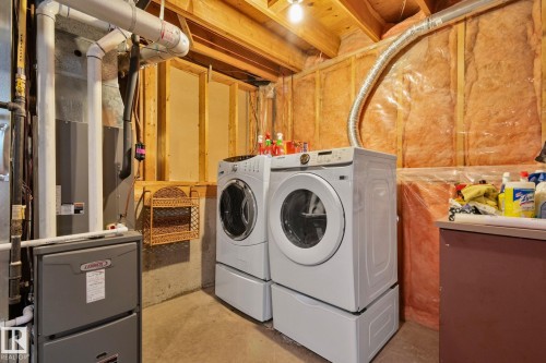 Laundry area with side-by-side washer and dryer units on pedestals, concrete flooring, exposed wood ceiling joists, and insulated wall framing - 18903 70 Avenue, Edmonton, AB - Indoor Photo Showing Laundry Room