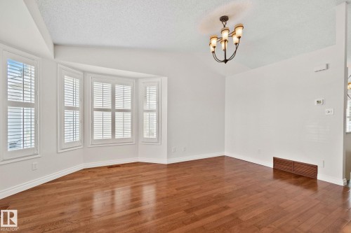 Living area featuring a bay window with plantation shutters, wood-finish flooring, a vaulted ceiling, and an ornate chandelier - 18903 70 Avenue, Edmonton, AB - Indoor Photo Showing Other Room
