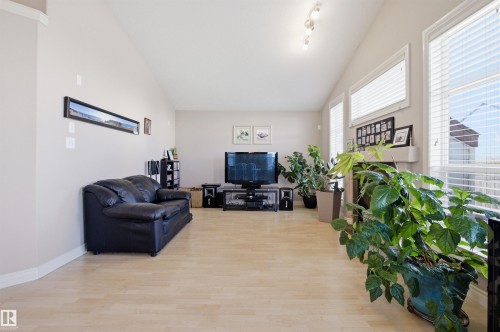 Living area featuring light wood-finish flooring, vaulted ceilings, multiple windows with blinds, a built-in fireplace with mantel, and track lighting - 16204 48 Street, Edmonton, AB - Indoor