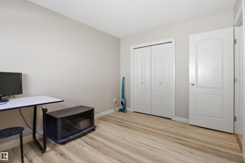 Room featuring wood-finish flooring, light neutral wall paint, white trim, and a white bi-fold closet door - 16204 48 Street, Edmonton, AB - Indoor Photo Showing Office