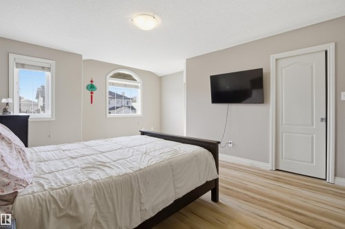 Spacious room featuring wood-finish flooring, two distinct window styles including an arched window, and a flush-mount ceiling light fixture - 16204 48 Street, Edmonton, AB - Indoor Photo Showing Bedroom
