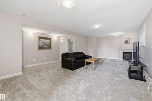 Spacious carpeted room featuring a corner fireplace with a white mantel, recessed lighting, and wall sconces - 16204 48 Street, Edmonton, AB - Indoor With Fireplace