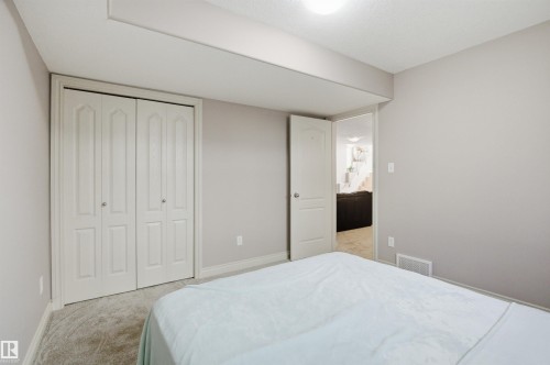 Carpeted room featuring light gray walls, white baseboards, and a white bi-fold closet door with decorative paneling and circular chrome hardware - 16204 48 Street, Edmonton, AB - Indoor Photo Showing Bedroom