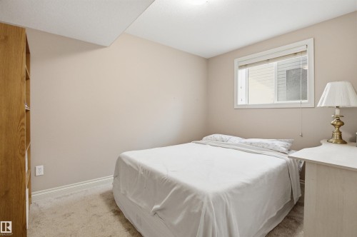 Carpeted room featuring a single window with blinds, light-toned walls, white trim, and a wood-finish built-in shelving unit - 16204 48 Street, Edmonton, AB - Indoor Photo Showing Bedroom