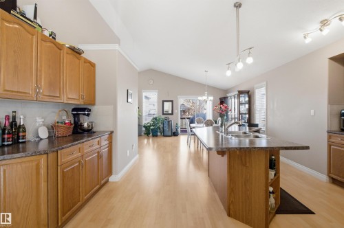 Kitchen featuring wood cabinetry, laminate countertops, light wood-finish flooring, a kitchen island with a double basin sink, and a track lighting fixture - 16204 48 Street, Edmonton, AB - Indoor Photo Showing Kitchen With Double Sink