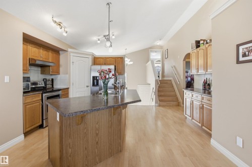 Kitchen featuring a central island with countertop seating, stainless steel appliances, wood-finish cabinetry, light wood-finish flooring, and vaulted ceilings - 16204 48 Street, Edmonton, AB - Indoor Photo Showing Kitchen
