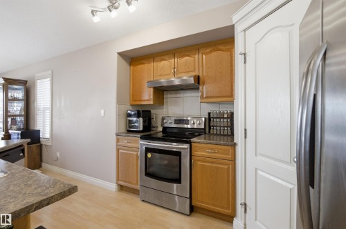 Kitchen featuring wood cabinetry, stainless steel appliances, neutral tile backsplash, and light wood-finish flooring - 16204 48 Street, Edmonton, AB - Indoor Photo Showing Kitchen