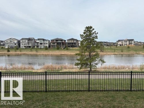 Waterfront property with an expansive lawn, black metal fencing, and a paved walking path - 5621 Cautley Cove, Edmonton, AB - Outdoor With Body Of Water With View