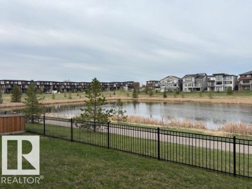 Lakeside property featuring a black metal fence, green lawn, and a wooden privacy fence section - 5621 Cautley Cove, Edmonton, AB - Outdoor With Body Of Water With View