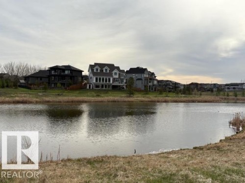 Waterside homes featuring varied architectural styles and private balconies, set against a natural landscape with mature vegetation - 5621 Cautley Cove, Edmonton, AB - Outdoor With Body Of Water With View