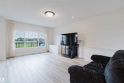 Spacious room featuring light wood-finish flooring, a large multi-pane window, and a built-in fireplace with a white mantel - 17718 5A Avenue, Edmonton, AB - Indoor Photo Showing Living Room