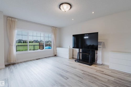 Spacious living area featuring large windows with grid accents, light wood-finish flooring, and a decorative fireplace with a stone surround and classic mantelpiece - 17718 5A Avenue, Edmonton, AB - Indoor Photo Showing Other Room