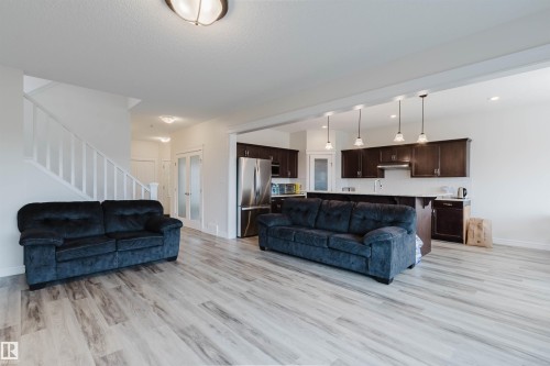 Open-concept living space featuring wood-finish flooring, a contemporary kitchen with dark cabinetry and stainless steel appliances, and a staircase with white railings - 17718 5A Avenue, Edmonton, AB - Indoor Photo Showing Living Room