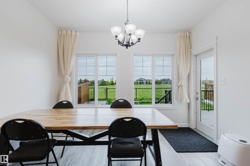 Dining area featuring a contemporary chandelier, two large windows, and a glass-paneled exterior door - 17718 5A Avenue, Edmonton, AB - Indoor Photo Showing Dining Room