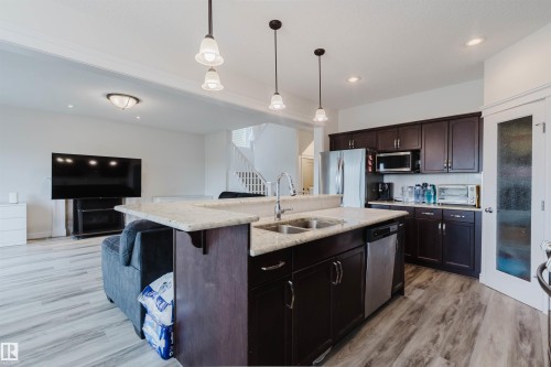 Open-concept kitchen featuring dark wood-finish cabinetry, a light-toned countertop, and stainless steel appliances - 17718 5A Avenue, Edmonton, AB - Indoor Photo Showing Kitchen With Double Sink