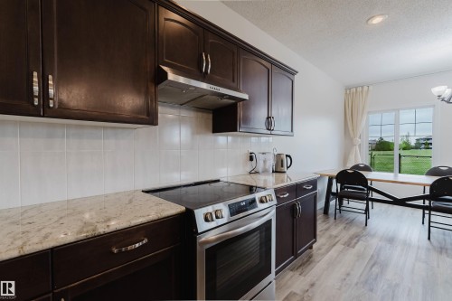 Kitchen featuring dark wood cabinetry, light-toned countertops, a stainless steel range with overhead ventilation, and white tile backsplash - 17718 5A Avenue, Edmonton, AB - Indoor Photo Showing Kitchen With Upgraded Kitchen