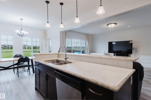 Kitchen island featuring a double basin stainless steel sink, a chrome gooseneck faucet, and light-toned stone countertops - 17718 5A Avenue, Edmonton, AB - Indoor Photo Showing Kitchen With Double Sink