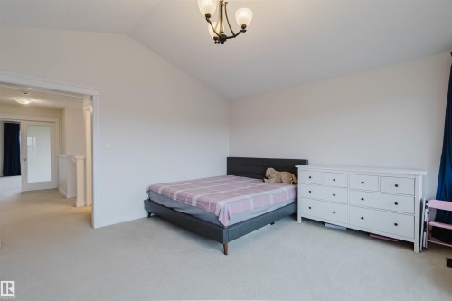 Spacious room featuring vaulted ceilings, neutral carpeting, and an open doorway providing access to a hallway with a frosted glass door - 17718 5A Avenue, Edmonton, AB - Indoor Photo Showing Bedroom