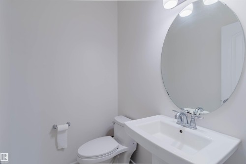 Contemporary pedestal sink with chrome faucet, circular mirror, and overhead vanity lighting - 17718 5A Avenue, Edmonton, AB - Indoor Photo Showing Bathroom