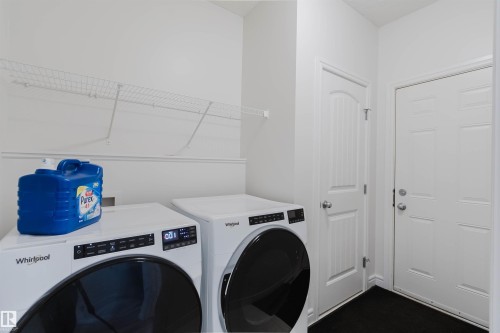 Dedicated laundry area featuring a front-loading washer and dryer, overhead wire shelving, and two white panel doors - 17718 5A Avenue, Edmonton, AB - Indoor Photo Showing Laundry Room