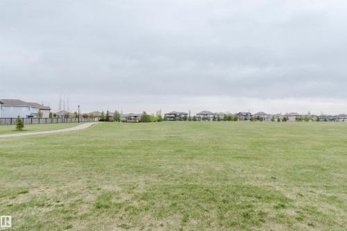 Expansive green space featuring a paved walking path, surrounding residential properties, scattered trees, and a decorative fence line - 17718 5A Avenue, Edmonton, AB - Outdoor With View