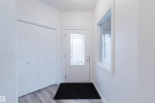 Entryway featuring a white door with decorative glass inserts, a single pane window, bi-fold closet doors, and wood-finish flooring - 17718 5A Avenue, Edmonton, AB - Indoor Photo Showing Other Room
