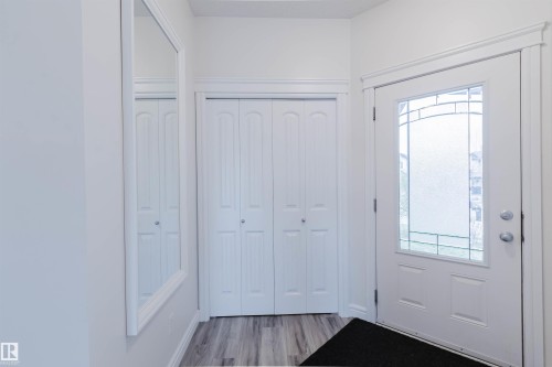 Entryway featuring a white front door with decorative glass inserts, bi-fold closet doors, a framed wall mirror, light wood-finish flooring, and white trim - 17718 5A Avenue, Edmonton, AB - Indoor Photo Showing Other Room