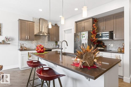 Modern kitchen featuring a large island with an undermount sink, pendant lighting, two-tone cabinetry, a herringbone tile backsplash, and stainless steel appliances - 7942 Erasmus Crescent, Edmonton, AB - Indoor Photo Showing Kitchen With Upgraded Kitchen
