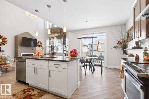 Open-concept living space featuring a central kitchen island with a dark countertop and stainless-steel appliances - 7942 Erasmus Crescent, Edmonton, AB - Indoor Photo Showing Kitchen With Upgraded Kitchen