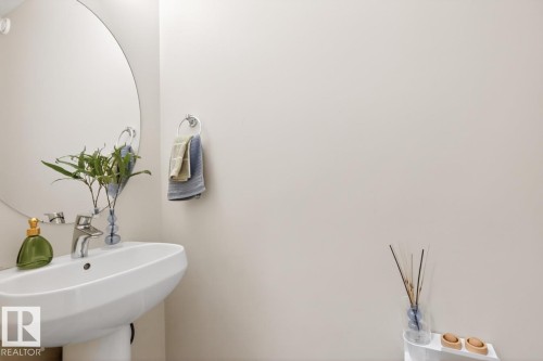 Pedestal sink with chrome faucet, large circular mirror, and chrome towel ring - 7942 Erasmus Crescent, Edmonton, AB - Indoor Photo Showing Bathroom