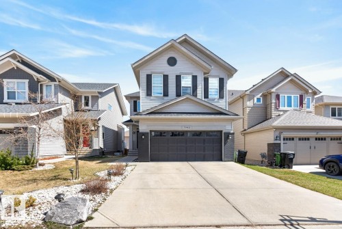 Two-story residence featuring light-toned horizontal siding, a prominent front-facing gable, and a two-car garage with a dark panel door - 7942 Erasmus Crescent, Edmonton, AB - Outdoor With Facade