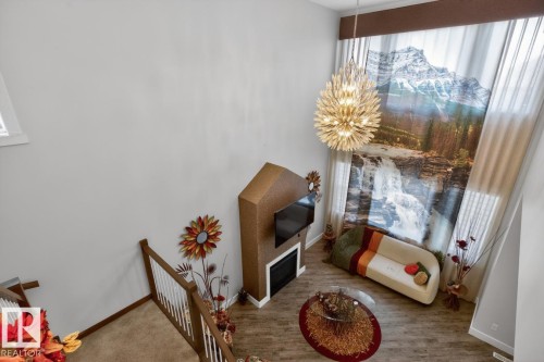 Two-story living area featuring a prominent floor-to-ceiling mural, a contemporary chandelier, and wood-finish flooring - 7942 Erasmus Crescent, Edmonton, AB - Indoor Photo Showing Other Room