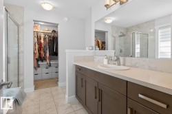 Bathroom featuring a spacious walk-in closet, a vanity with ample counter space, a large mirror, a glass-enclosed shower, and tile flooring - 