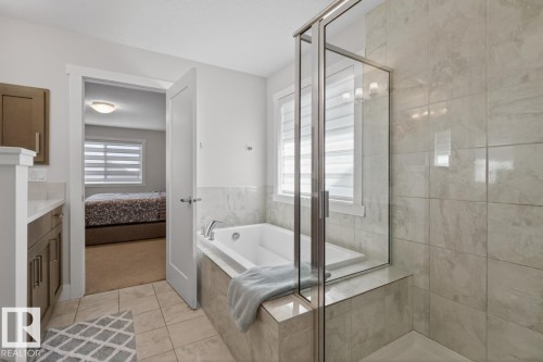 Bathroom featuring a glass-enclosed shower, a built-in soaking tub with deck-mounted fixtures, and light-toned tile flooring - 7942 Erasmus Crescent, Edmonton, AB - Indoor Photo Showing Bathroom
