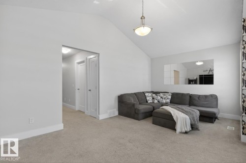Living area with vaulted ceiling, neutral carpeting, and a hallway featuring white paneled doors - 7942 Erasmus Crescent, Edmonton, AB - Indoor