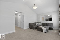 Living area with vaulted ceiling, neutral carpeting, and a hallway featuring white paneled doors - 