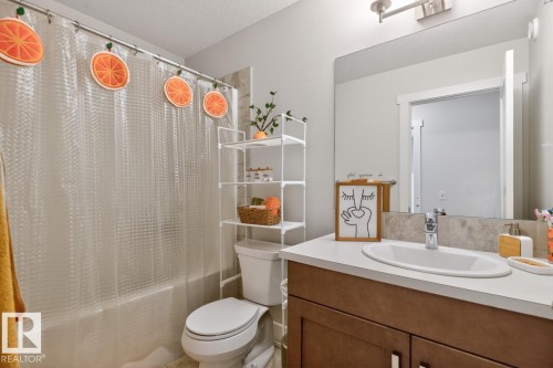 Bathroom featuring a white toilet, full-sized bathtub with a clear shower curtain, and an over-toilet storage unit - 7942 Erasmus Crescent, Edmonton, AB - Indoor Photo Showing Bathroom