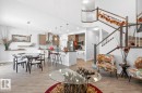Open-concept living area featuring wood-finish flooring, a contemporary kitchen with stainless steel appliances, a kitchen island with seating, a dining area, and a staircase with wood railings - 7942 Erasmus Crescent, Edmonton, AB  - Indoor 