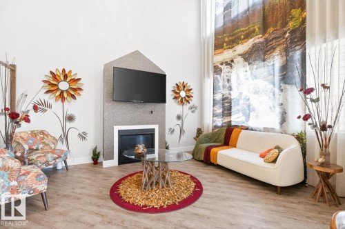 Spacious living area featuring high ceilings, wood-finish flooring, a contemporary fireplace with a mounted television, and large windows with privacy drapes - 7942 Erasmus Crescent, Edmonton, AB - Indoor Photo Showing Living Room With Fireplace