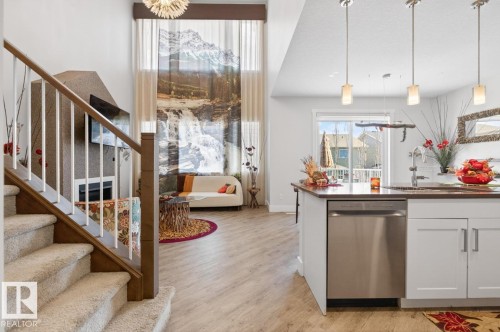 Open-concept living space featuring wood-finish flooring, a contemporary fireplace, and a kitchen island with built-in stainless steel appliances - 7942 Erasmus Crescent, Edmonton, AB - Indoor