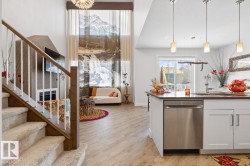 Open-concept living space featuring wood-finish flooring, a contemporary fireplace, and a kitchen island with built-in stainless steel appliances - 