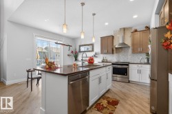 Kitchen featuring a central island with integrated dishwasher, stainless steel appliances, two-tone cabinetry, herringbone tile backsplash, and wood-finish flooring - 