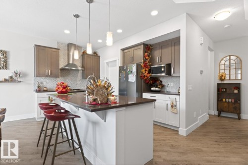 Kitchen featuring a central island with countertop seating, wood-finish flooring, two-tone cabinetry, stainless steel appliances, and pendant lighting - 7942 Erasmus Crescent, Edmonton, AB - Indoor Photo Showing Kitchen With Upgraded Kitchen